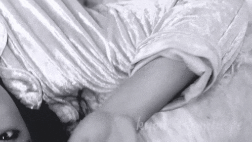 a black and white photo of a woman laying on a bed with a white shirt on