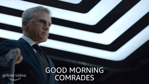 a man in a suit and tie is holding a suitcase and says " good morning comrades "