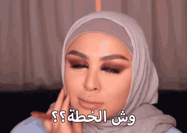 a woman wearing a hijab is applying makeup and has arabic writing above her face