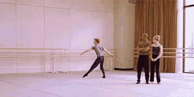 a man and a woman are standing next to each other in a dance studio while a man is dancing .