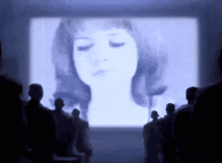 a group of people are looking at a woman 's face on a screen