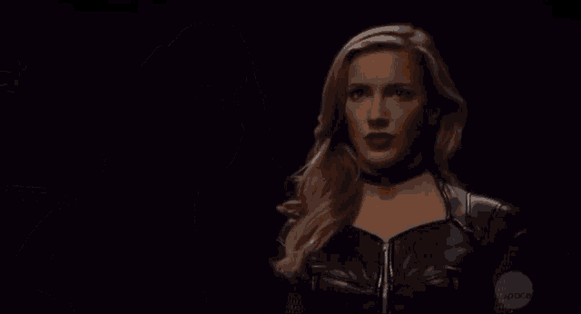a woman in a black costume is holding a sword in a dark room .