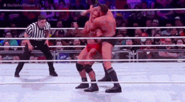two men are wrestling in a wrestling ring with a referee watching .