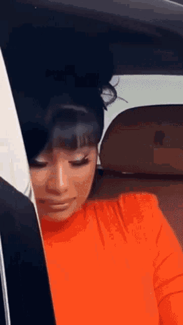 a woman in an orange shirt is sitting in a car with her eyes closed .
