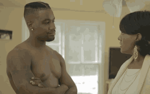 a shirtless man standing next to a woman in a living room .