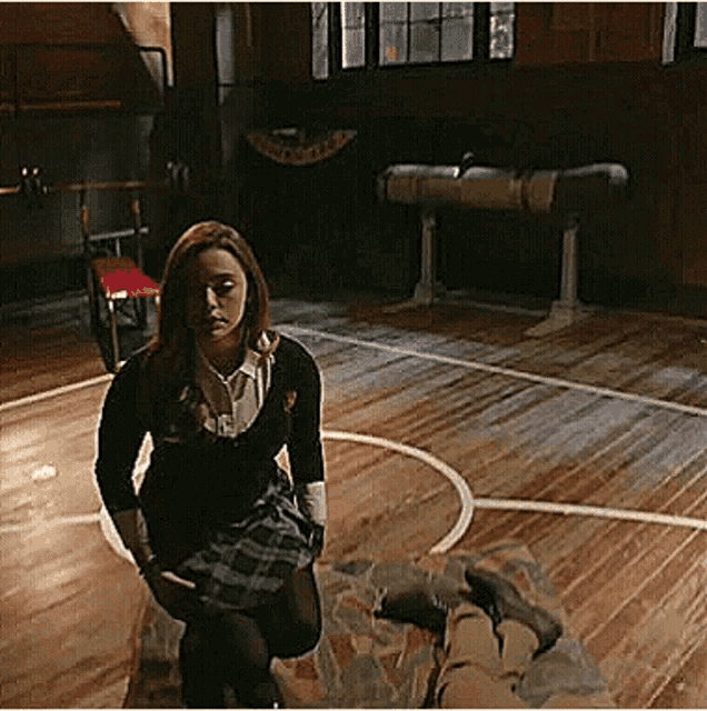 a woman in a plaid skirt is kneeling down in a gym .