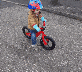 a young boy wearing a helmet and gloves is riding a red bicycle