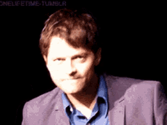 a man in a suit and a blue shirt is making a funny face .
