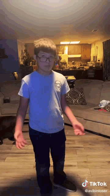 a young boy is standing in a living room wearing glasses and a blue shirt .