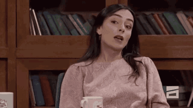 a woman in a pink shirt is sitting at a table with a cup of coffee .