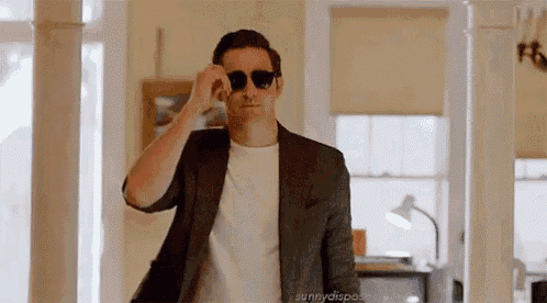 a man wearing sunglasses and a suit is standing in a hallway .
