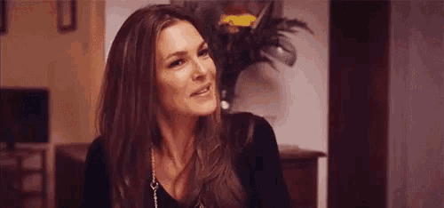 a woman with long brown hair is smiling and looking at the camera while sitting in a living room .