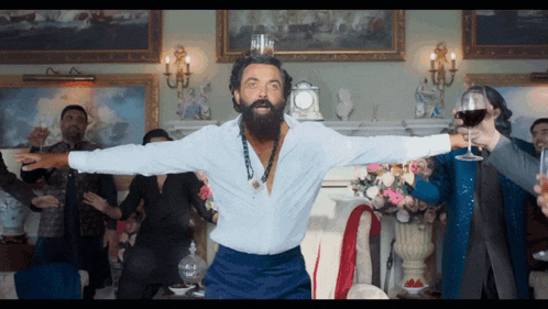 a man with a beard is dancing with his arms outstretched in a room full of people