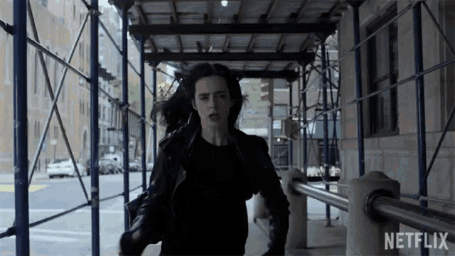 a woman in a black leather jacket is running down a sidewalk with a netflix logo in the corner