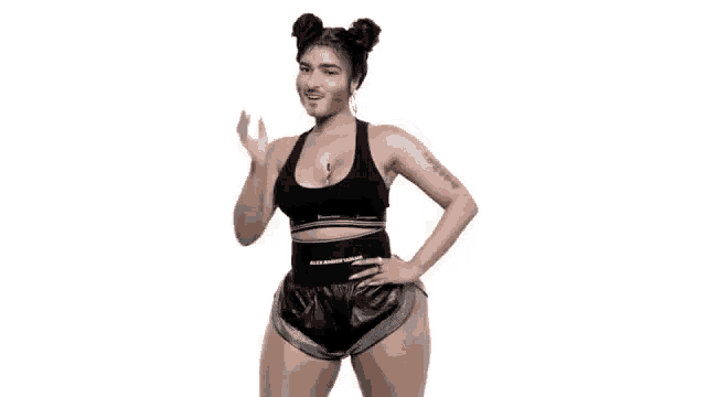 a woman in a black top and shorts is standing with her hand on her hip .