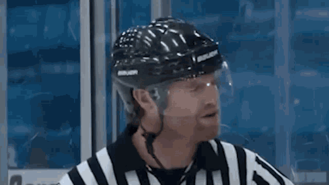 a hockey referee wearing a helmet and a striped shirt is standing in front of a glass door .