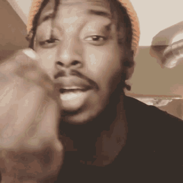 a man with dreadlocks and a beard is wearing an orange hat and making a funny face .