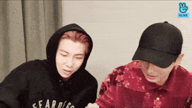 a man wearing a black hoodie with the word fear on it stands next to another man wearing a red shirt with flowers on it