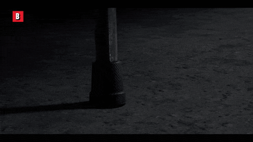 a black and white photo of a person standing in the dark with a red b in the corner .