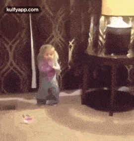 a little girl is standing on a wooden floor in a living room next to a lamp .