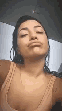 a woman in a pink tank top is making a funny face while taking a selfie .