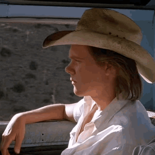 a man wearing a cowboy hat and white shirt looks out a window