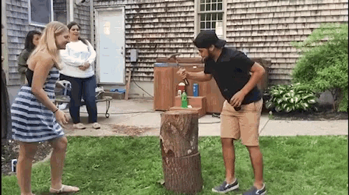 a man is standing next to a tree stump while a woman in a striped dress watches .