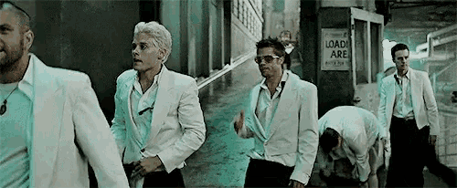 a group of men in white suits are walking down a sidewalk .