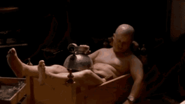 a bald man with a mustache is laying in a wooden box with his eyes closed .