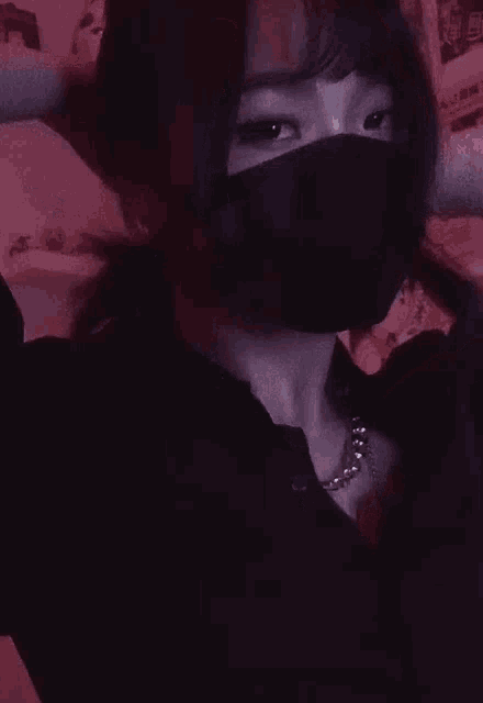 a girl wearing a black mask and a necklace is standing in front of a pink wall .
