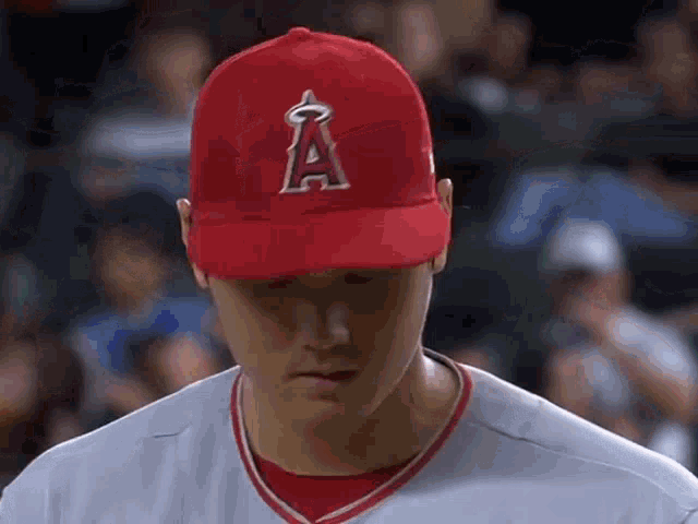 a baseball player wearing a red hat with the letter a on it is looking down .