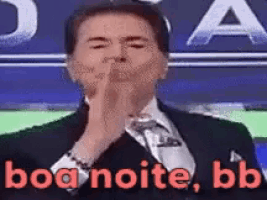 a man in a suit and tie is blowing a kiss in front of a sign that says boa noite