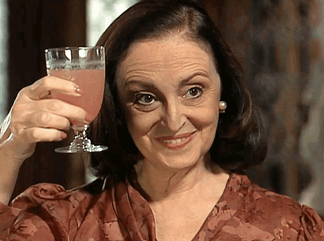 a woman holds up a glass of pink liquid in her hand
