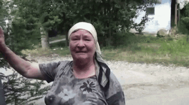 an elderly woman wearing a head scarf is standing on the side of a road .
