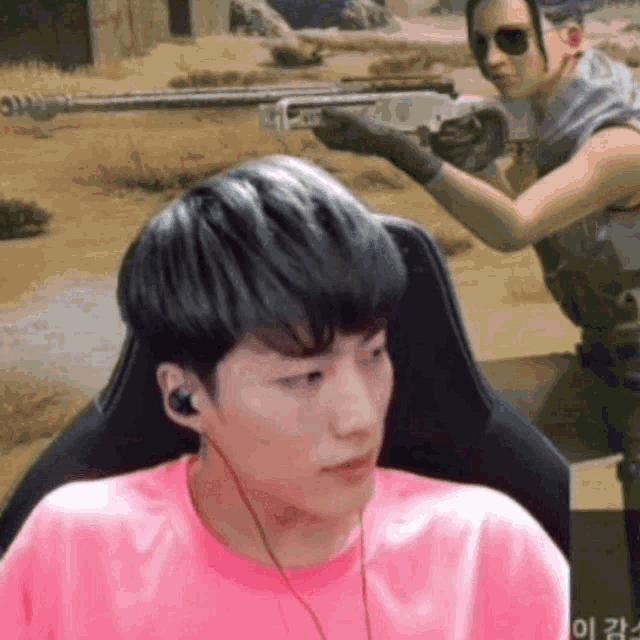a man in a pink shirt is sitting in a chair while a man with a gun stands behind him .