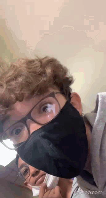 a man wearing glasses and a black mask is standing next to a woman wearing a white mask .