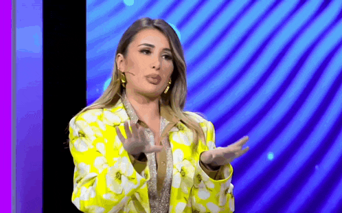 a woman in a yellow and white floral jacket is standing in front of a microphone .
