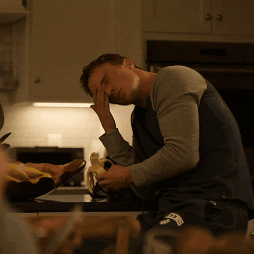 a man sitting at a kitchen counter eating a banana and wearing a shirt that says ' nyc ' on it