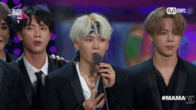 a group of young men are standing in front of a microphone with a mnet logo behind them