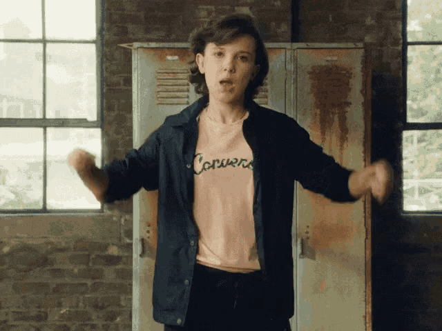 a girl wearing a converse shirt is dancing in front of lockers