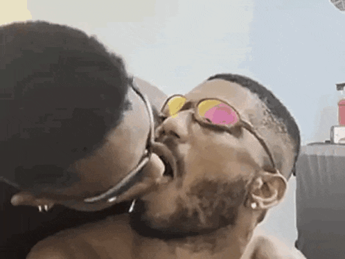 a man with glasses is kissing another man on the cheek .