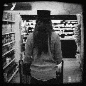 a woman wearing a top hat is pushing a shopping cart in a grocery store aisle .