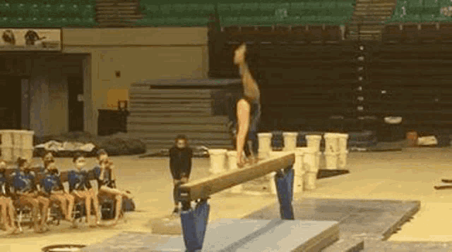 a gymnast is doing a trick on a balance beam in a gym while a group of people watch .