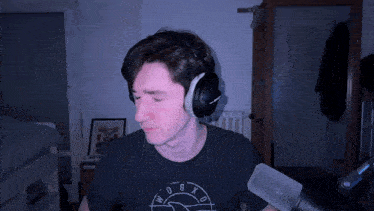 a man wearing headphones and a t-shirt with a clock on it stands in front of a microphone