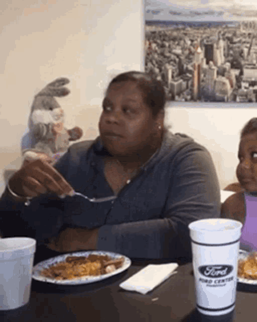 a woman is sitting at a table with a plate of food and a ford cup