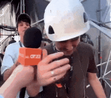 a man wearing a white hard hat is being interviewed by a reporter