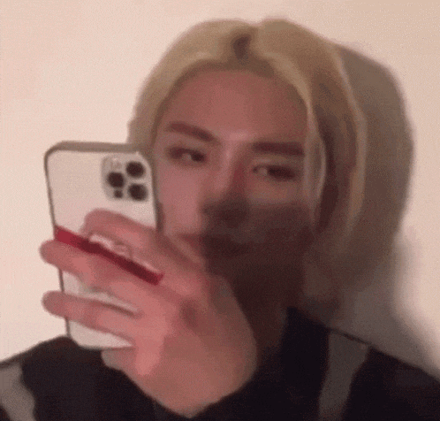 a man with blonde hair is taking a selfie with his cell phone .