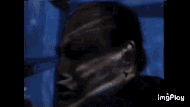 a close up of a person 's face in a dark room with a blue light behind them .