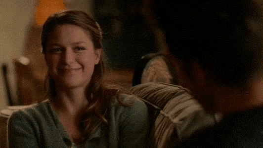 a woman is sitting on a couch with a man and smiling at him .