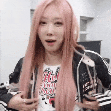 a woman with long pink hair is wearing a jacket and a t-shirt with the word hot on it .